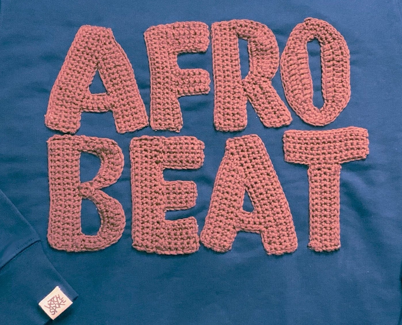 Close-up of the applique "AFROBEAT" text, highlighting the detailed and colourful embroidery.