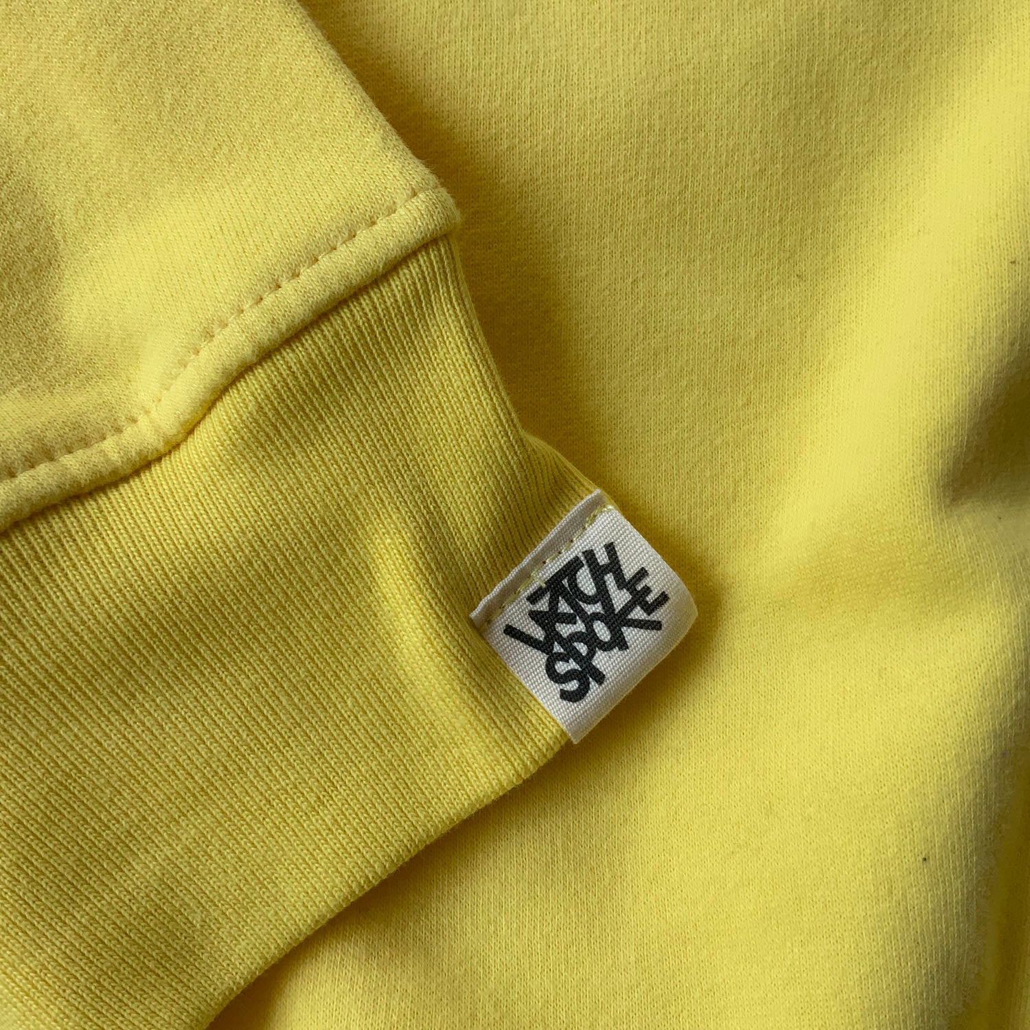 close up of a yellow sweatshirt sleeve with a white and black Latchspoke label